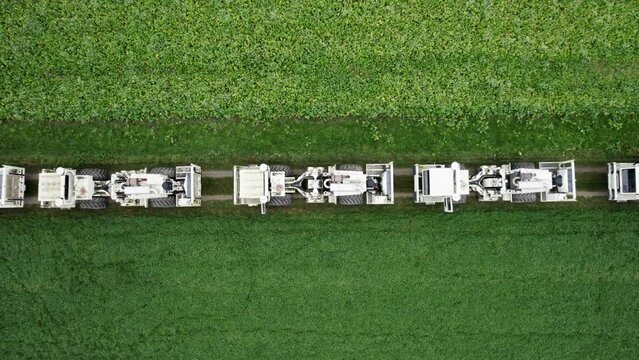 High Resolution Video of several Vibro-Truck shot with a drone. It shows several trucks lined up behind each other on a field. The drone flies up higher during the shot.