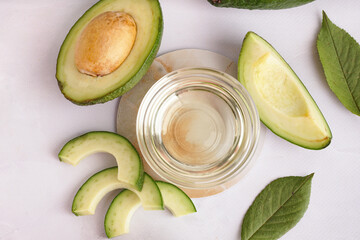 Fresh avocados, leaves and glass bowl with essential oil on white background