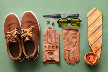 Set of stylish male accessories with leather gloves on green background