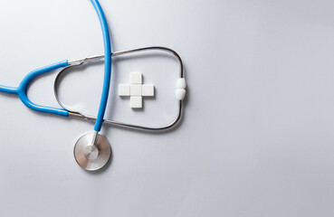 Blue stethoscope and white cross made of plastic bloсks on gray background. Medical insurance concept. Selective focus, copy space
