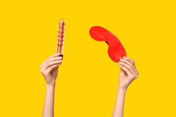 Female hands with vibrator and mask from sex shop on yellow background