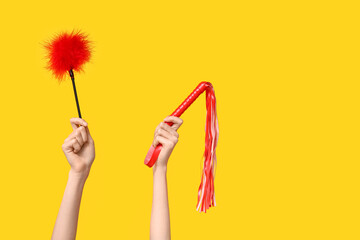 Female hands with feather stick and and whip from sex shop on yellow background