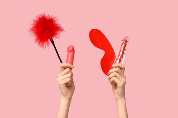 Female hands with vibrators, feather stick and mask from sex shop on pink background