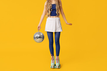 Beautiful young woman in vintage roller skates with disco ball on yellow background, closeup
