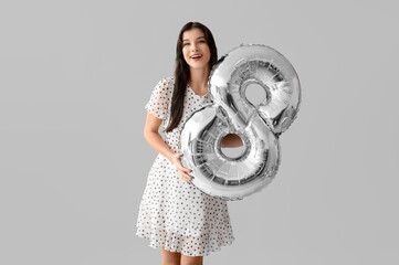 Happy young woman with silver air balloon in shape of figure 8 on grey background. International...