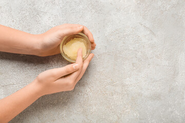 Female hands with bowl of body scrub on color background, closeup