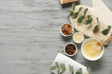 Composition with different body scrubs, bath supplies and eucalyptus branches on grey wooden background