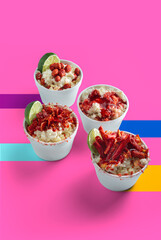 Group of Mexican snacks, various corns in cups, prepared with chili, peanuts, chips, chamoy sauce, on a background of Mexican colors, pastel pink