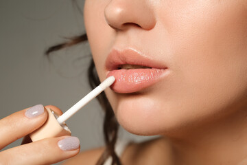 Naklejka premium Beautiful young woman applying lipgloss on grey background, closeup