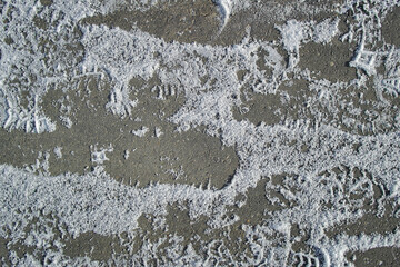 Background texture of gray asphalt. White snow. Human footprints. Closeup road surface. Gray road for background or texture