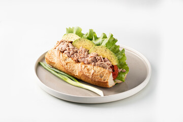 Appetizing sandwich with hard boiled egg, fresh lettuce, tuna and tomatoes served on baking paper on chopping wooden board on white background 