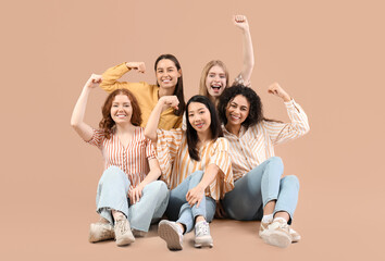 Obraz premium Beautiful young women with clenched fists sitting on beige background. Women history month