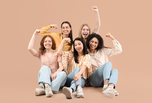 Beautiful young women with clenched fists sitting on beige background. Women history month