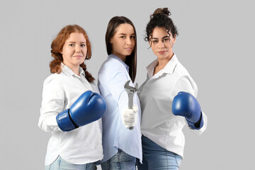 Young women in boxing gloves with adjustable wrench on grey background. Women history month