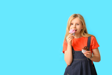 Cute little girl eating cupcakes on blue background