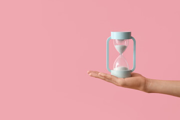 Female hand holding hourglass on pink background
