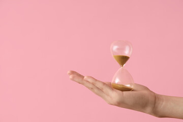 Female hand holding hourglass on pink background