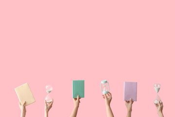 Female hands holding hourglasses and books on pink background