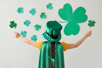 Funny girl with leprechaun's hat, cape and clovers near white wall, back view. St. Patrick's Day...
