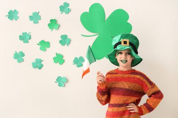 Funny girl with face painting, leprechaun's hat, flag of Ireland and clovers near white wall. St....
