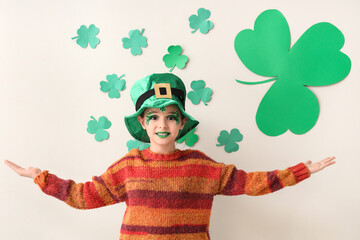 Funny girl with face painting, leprechaun's hat and clovers near white wall. St. Patrick's Day...