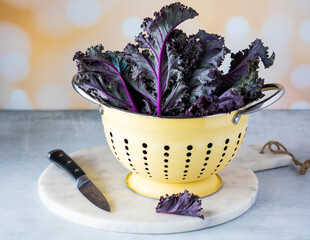 A close up of purple kale in a yellow colander, on a marble slab.