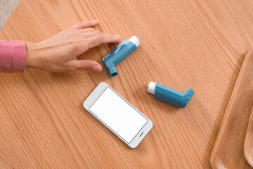 Young woman with asthma inhalers and mobile phone on table, top view