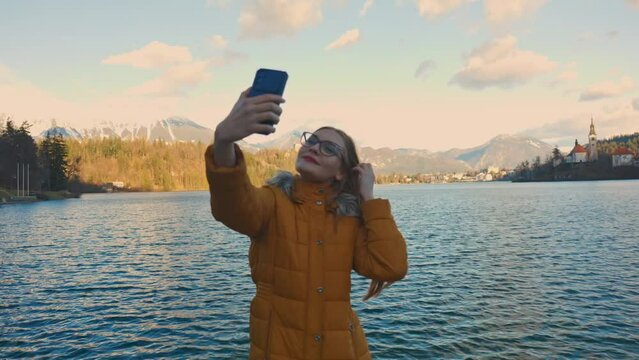 4K video of a beautiful young caucasian female taking a selfie photo at a very famous touristic destination Bled, Slovenia.