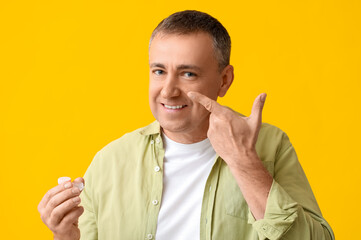 Mature man putting in contact lenses on yellow background