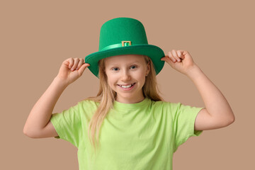 Cute little girl in leprechaun hat on brown background. St. Patrick's Day celebration