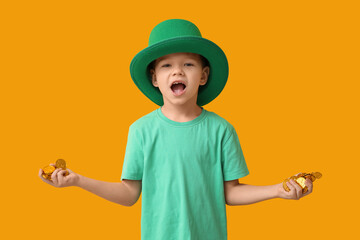 Cute little boy in leprechaun hat with coins on yellow background. St. Patrick's Day celebration