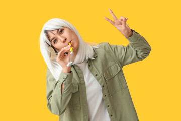 Beautiful young woman in funny disguise with party whistle showing silent gesture on yellow...