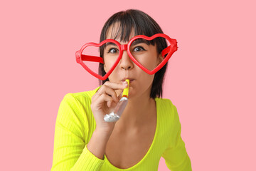 Beautiful young woman in funny disguise with party whistle on pink background. April Fools Day...