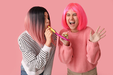 Beautiful young women in wigs with whistles on pink background. April Fools Day celebration
