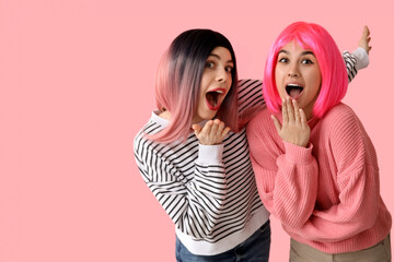 Beautiful young shocked women in wigs on pink background. April Fools Day celebration