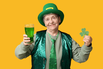 Senior woman in leprechaun hat with glass of beer and clover on yellow background. St. Patrick's...
