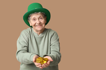 Senior woman in leprechaun hat with coins on brown background. St. Patrick's Day celebration
