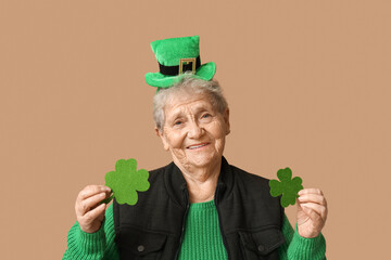 Senior woman in leprechaun hat with clover on brown background. St. Patrick's Day celebration