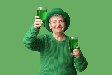 Senior woman in leprechaun hat with glasses of beer on green background. St. Patrick's Day...