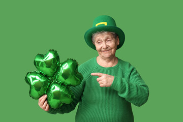 Senior woman in leprechaun hat pointing at air balloon in shape of clover on green background. St....