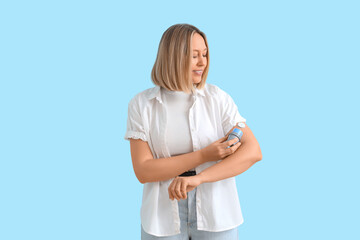 Diabetic woman with glucose sensor measuring blood sugar level on blue background