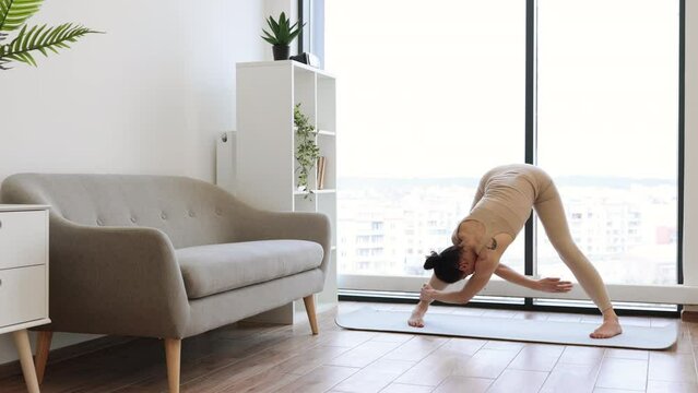 Caucasian woman squatting with feet shoulder width apart, holding hands on hips and twisting torso down into sides. Flexible brunette practising asana pose during yoga exercise at studio.