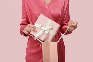 Young woman with shopping bag and gift box on pink background. International Women's Day