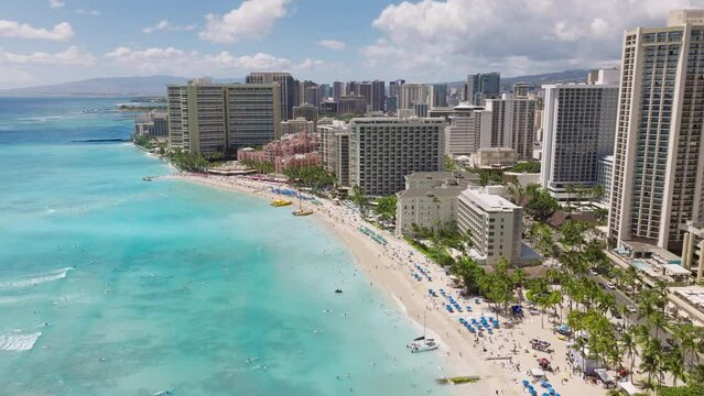 Honolulu city aerial 4K, Impressive travel destination copy background. Breathtaking views on delight light teal blue ocean at Waikiki beach. Modern city at blue sea with green mountains on background