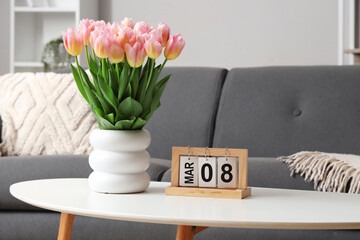 Calendar with date of International Women's Day and tulips on table in modern living room