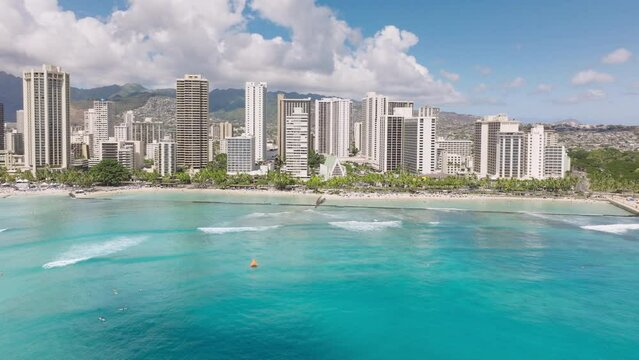 Impressive travel destination copy background. Breathtaking views on delight light teal blue ocean at Waikiki beach. Modern city at blue sea with green mountains on background. Honolulu city aerial 4K