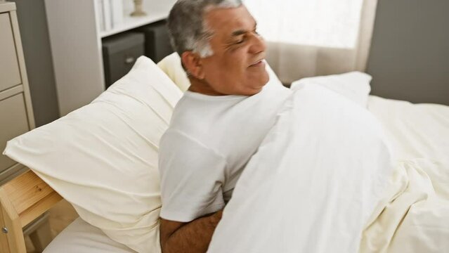 A middle-aged man with grey hair stretches joyfully in bed, capturing a sense of wellbeing in a cozy bedroom setting.