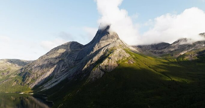 Barren mountain peak with grassy slope overlooks lake as clouds gather at top, Stetind Norway