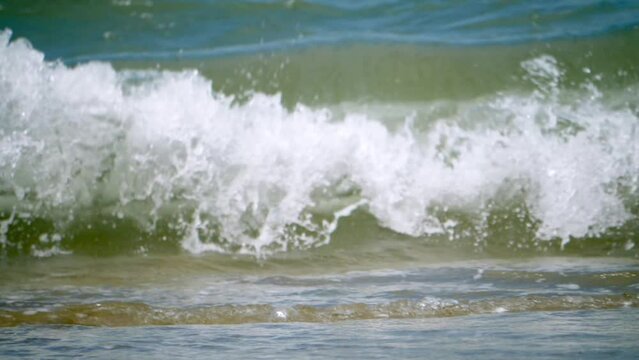 White, foamy waves rushing in and splashing at the sandy beachfront of a popular tourist destination in Chonburi province in Thailand.