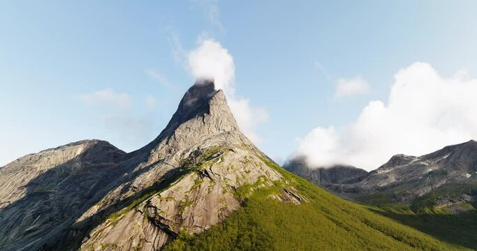 Clouds roll up on windward side of Stetind mountain peak in Norway, aerial orbit